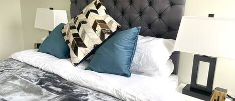 A neatly made bed with a patterned throw, blue pillows, and a tufted headboard.