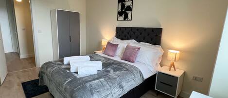 A modern bedroom with a large bed, bedside tables, a wardrobe, and a ceiling light.