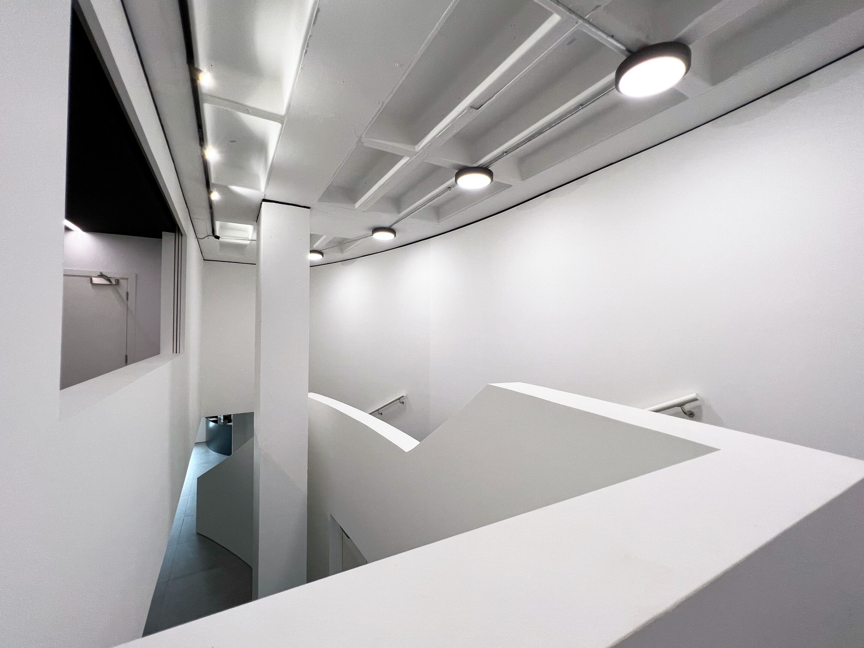 Ein modernes, minimalistisches Interieur mit weißen Wänden und Decke, eingelassener Beleuchtung und einer gebogenen weißen Arbeitsplatte.