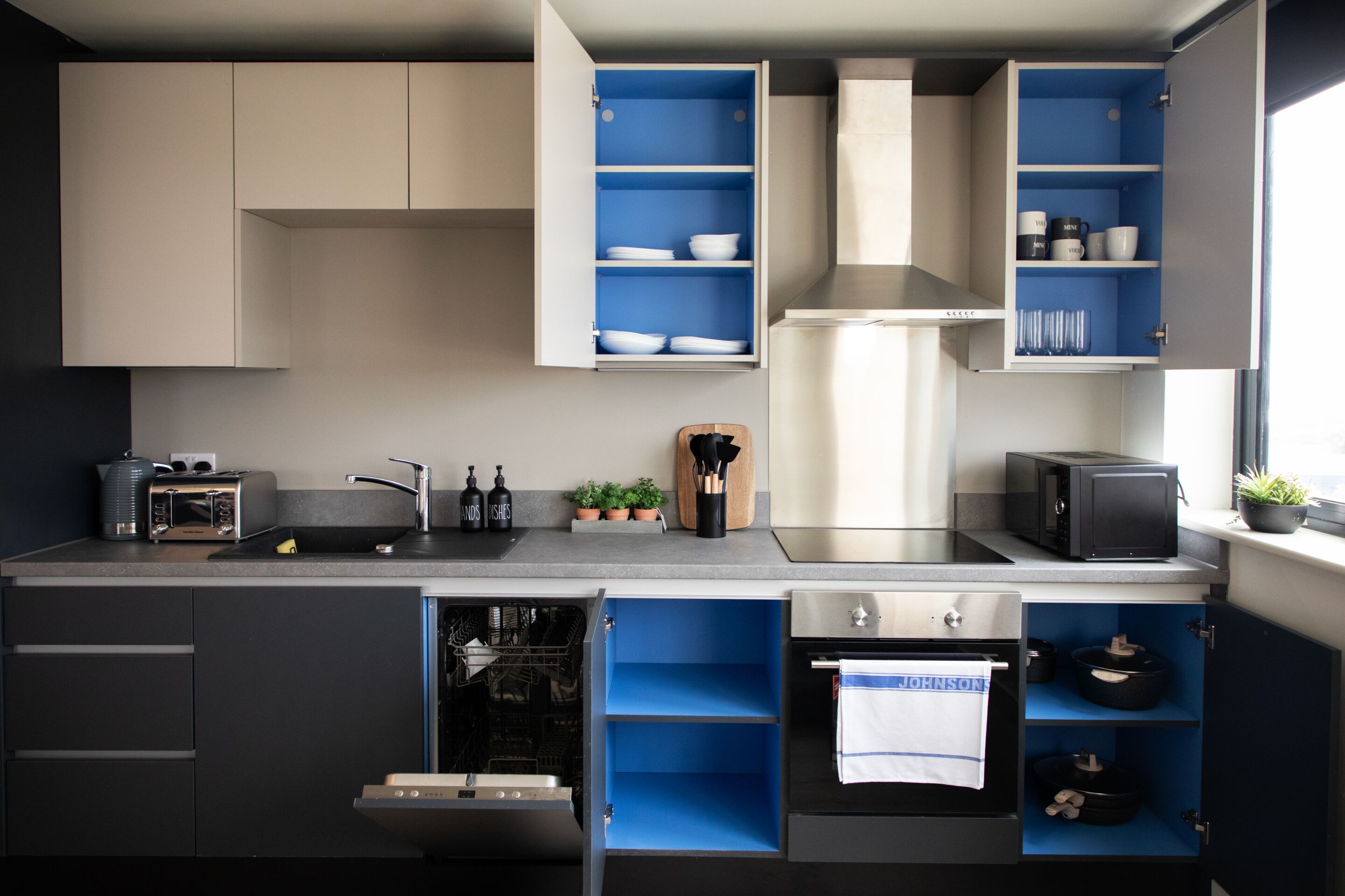 Une cuisine moderne avec des meubles gris, des étagères bleues, un four encastré et un four à micro-ondes.