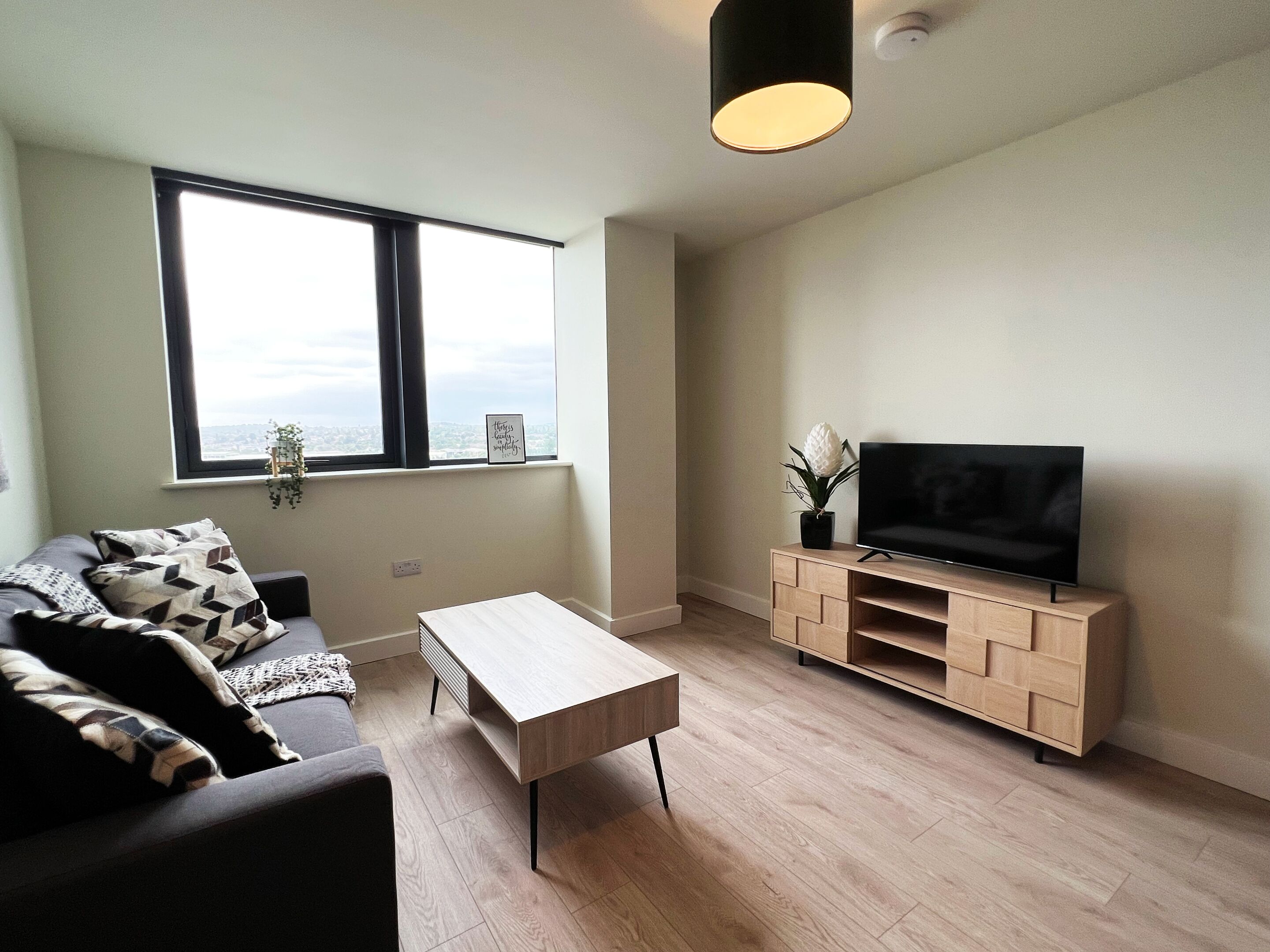 Ein modernes Wohnzimmer mit einer Couch, einem Couchtisch, einem Fernseher auf einem Holzboden und einem Fenster mit Blick auf die Stadt.