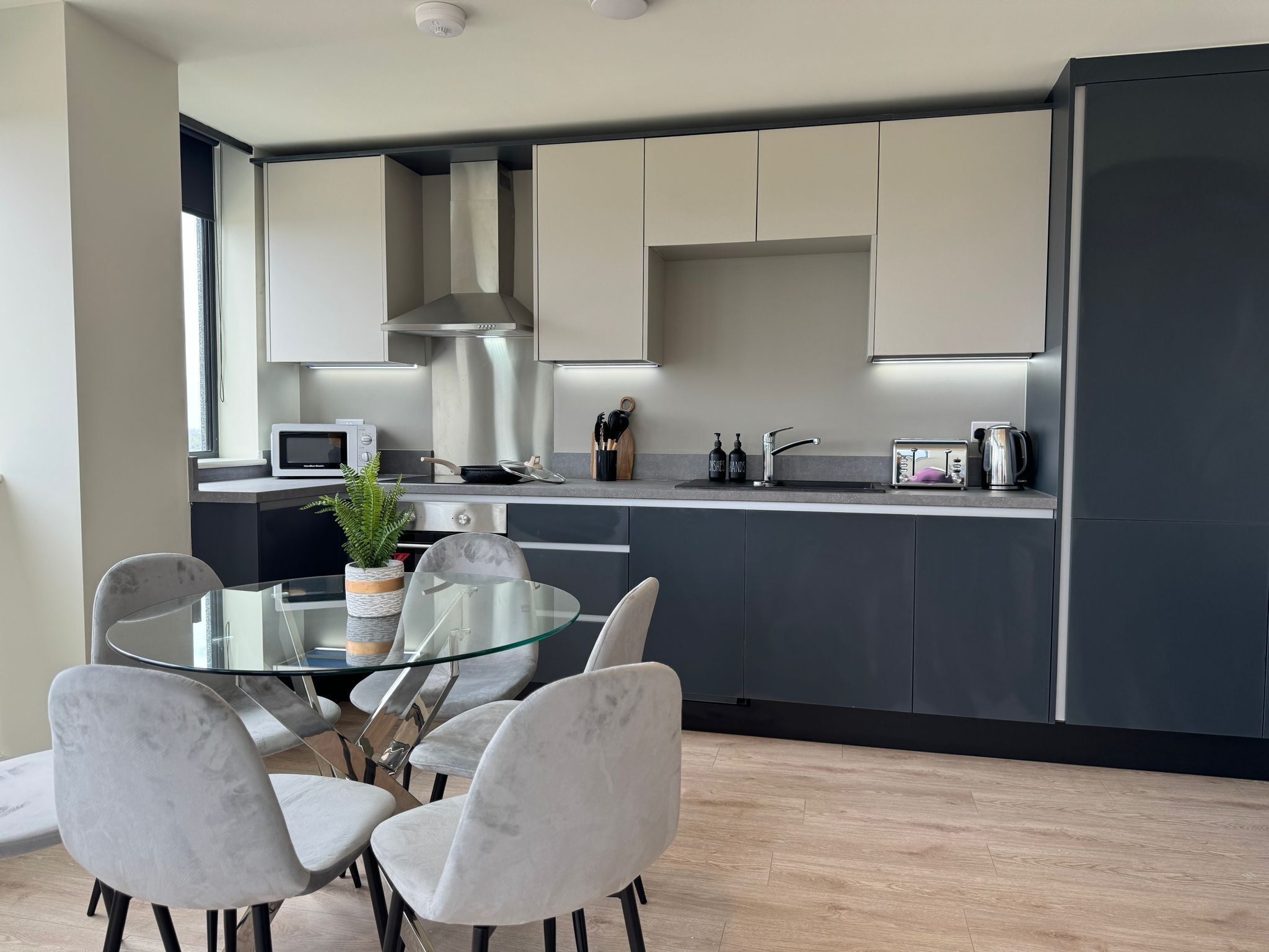 Et moderne køkken med et glas spisebord og stole, rustfrit stål hvidevarer og et minimalistisk design.