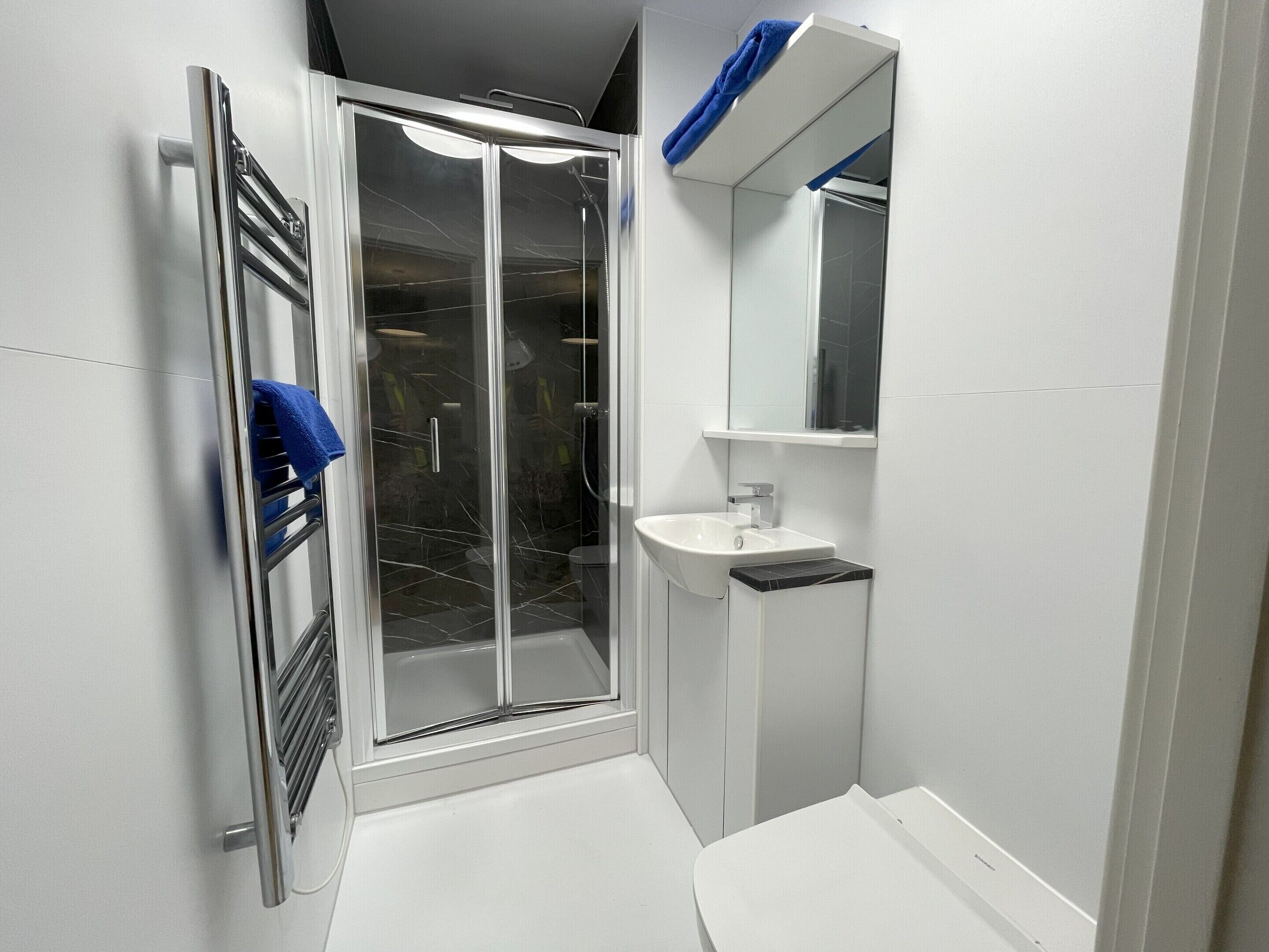 Un baño con cabina de ducha de vidrio, un lavamanos blanco y un espejo sobre él.