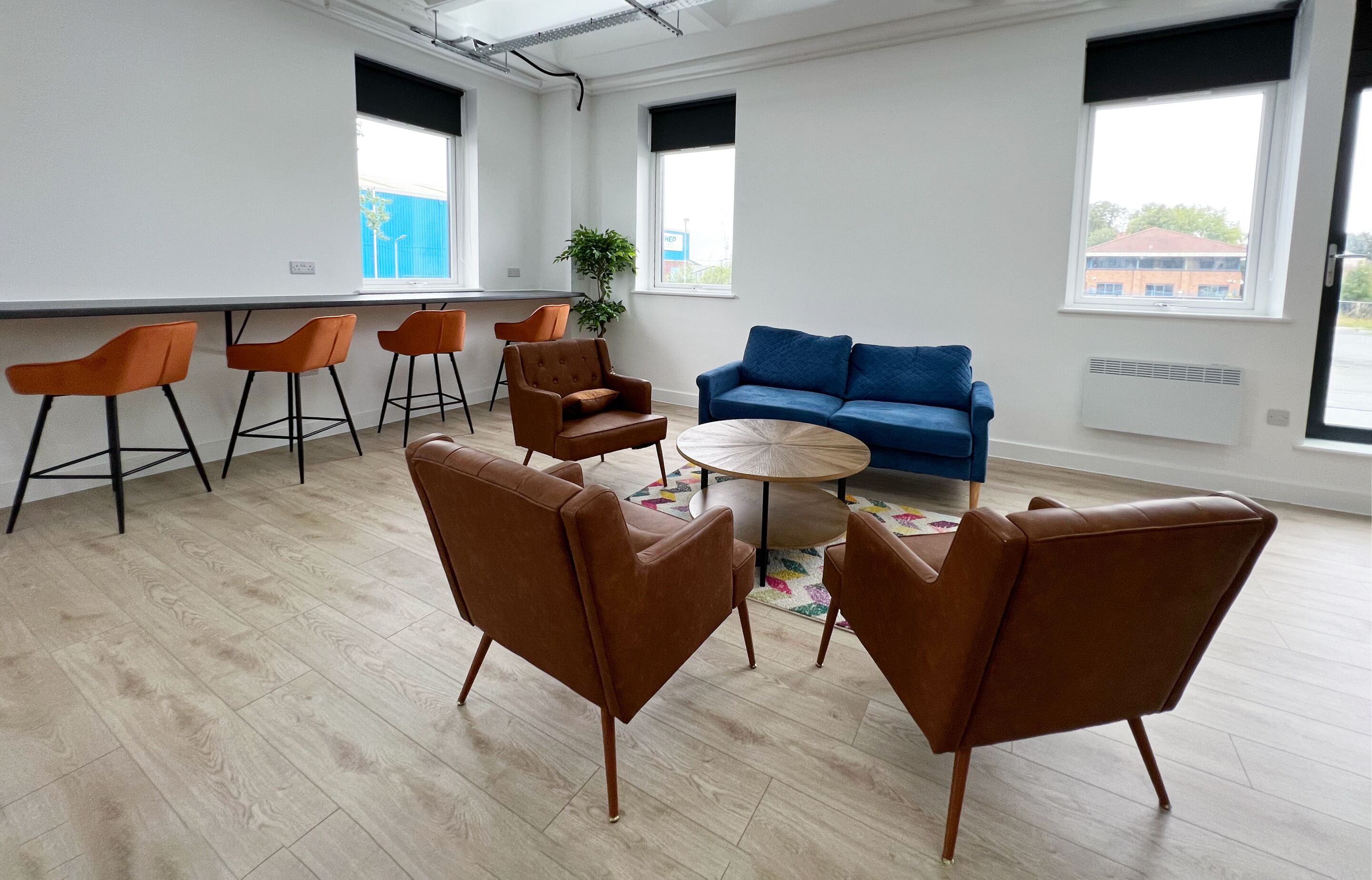 Un espacio de oficina moderno con un sofá azul, sillas marrones y una mesa redonda.