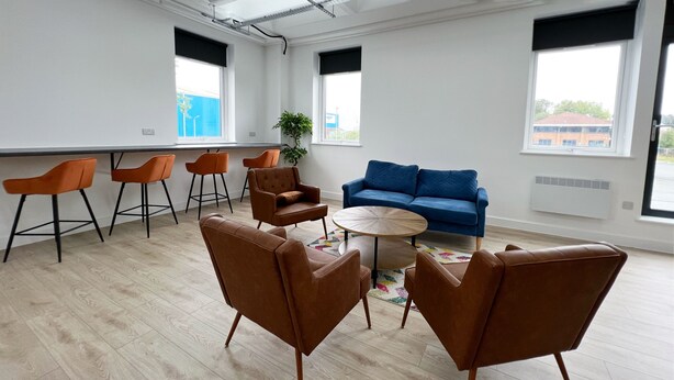 Un espacio de oficina moderno con un sofá azul, sillas marrones y una mesa redonda.
