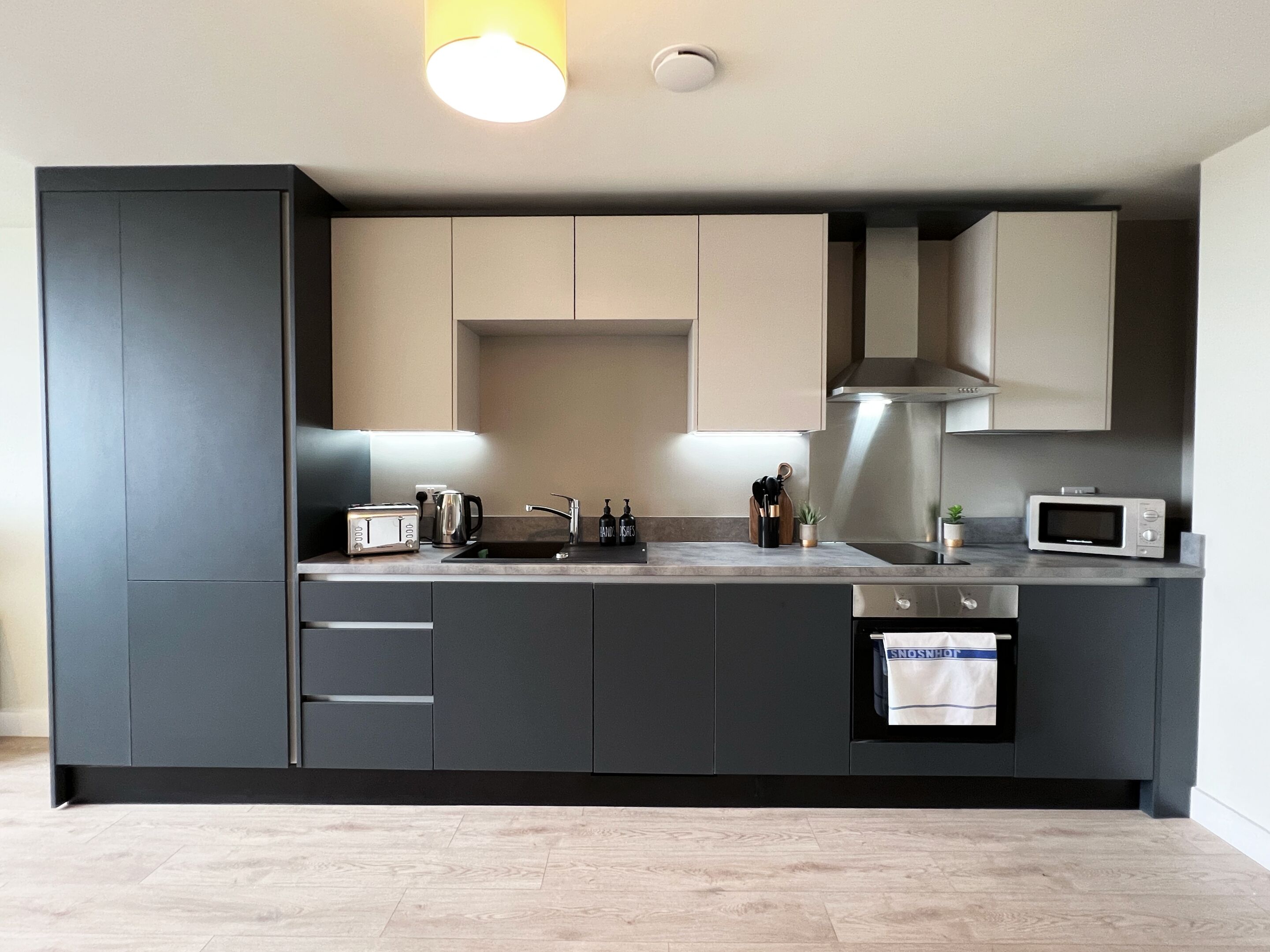 Una cocina moderna con armarios oscuros, un lavamanos de acero inoxidable, un microondas y un tostador.