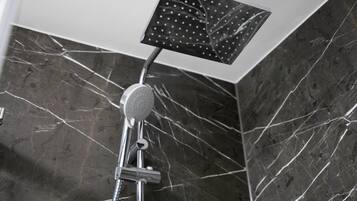 Una ducha moderna con cabezal cuadrado, accesorios de cromo y pared de mármol con vetas blancas.