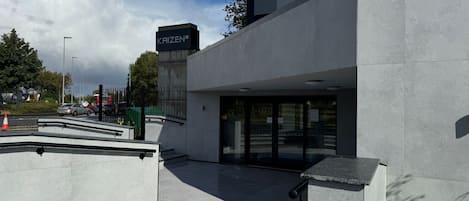 A modern building with a 'KAIZEN' sign, a covered entrance, and a paved area with steps leading to the entrance.