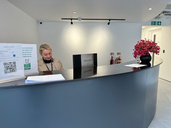 Een receptiebalie met een bord waarop contactgegevens bij nood, een QR-code en een bloevas staan.