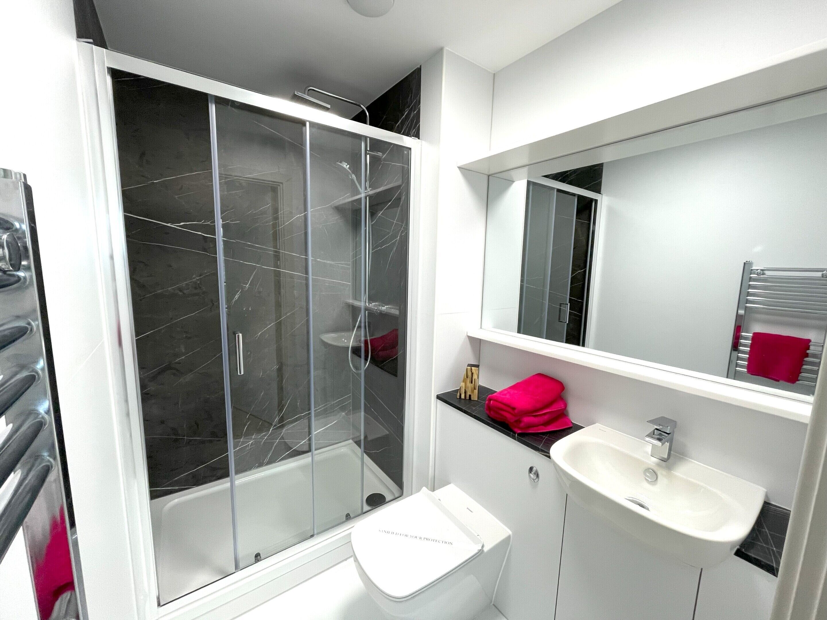 Un baño moderno con ducha envuelta en vidrio, un lavamanos blanco y un espejo sobre él.