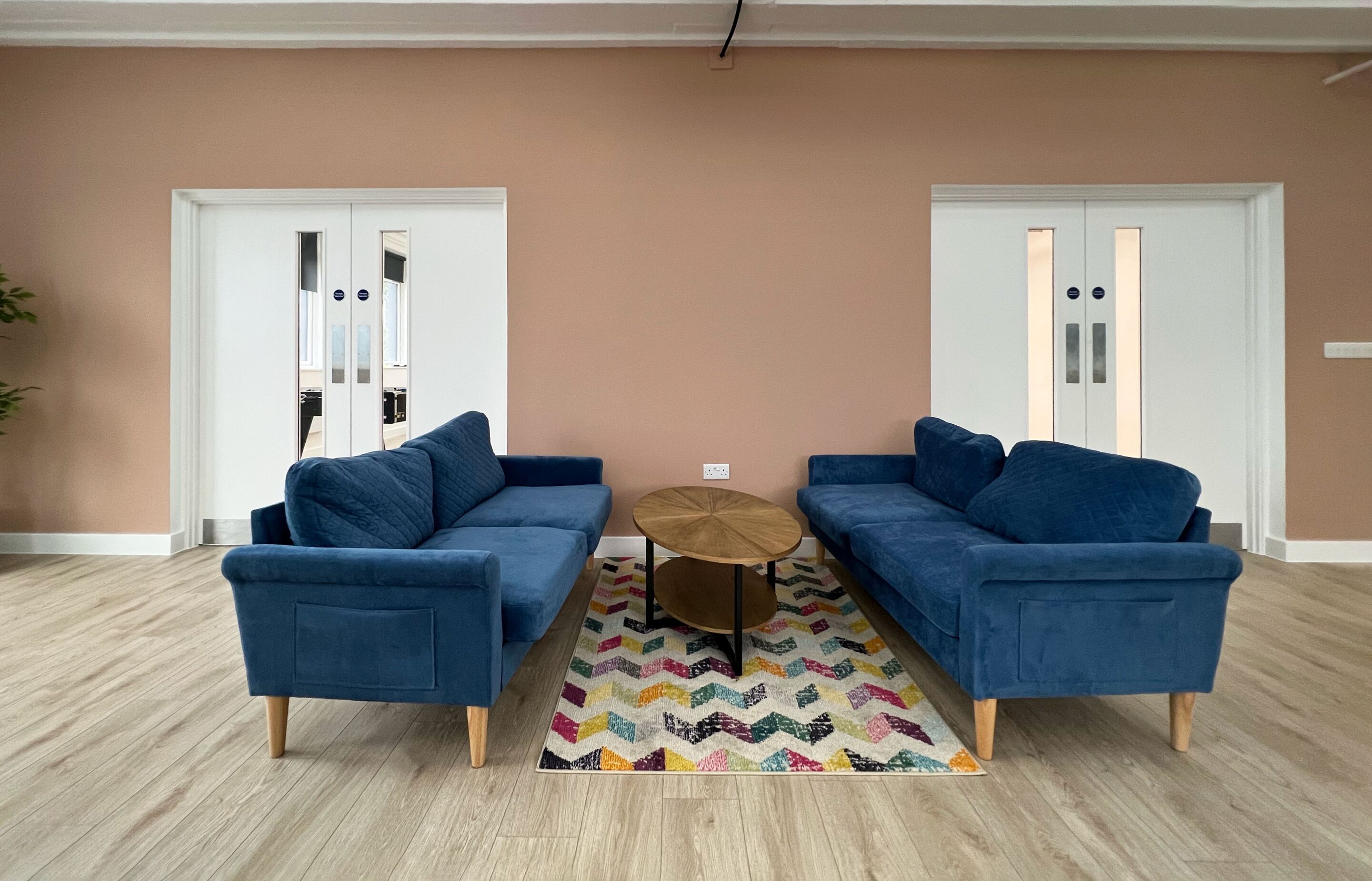 Ein Zimmer mit zwei blauen Sofas, einem kleinen Holztisch und einem farbenfrohen Teppich.