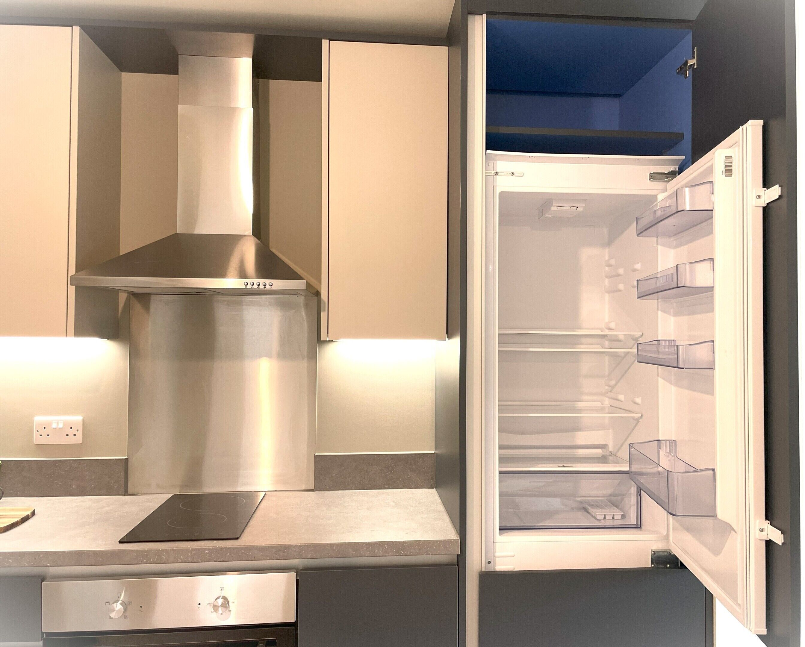 A modern kitchen with a stainless steel range hood, a built-in oven, and a refrigerator with clear storage bins.