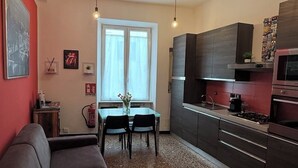 Moderni keittiö, jossa on tummat kaapit, ruokapöytä tuoleineen ja riippuvalaisimet.