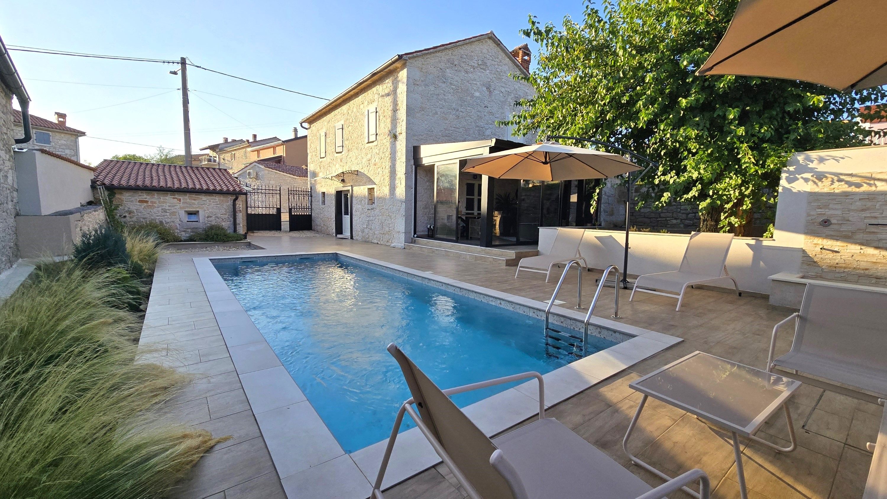 Une piscine bordée d’un muret en pierre, avec des chaises longues et un espace salon abrité.