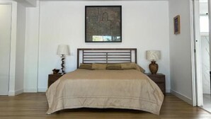 A bedroom with a bed, two bedside tables, a nightstand, a framed picture on the wall, and a door. - Quinta Verde Algarve (Faro)