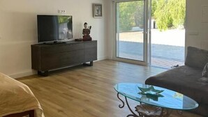 A spacious living room with a flat-screen TV, a dark wooden cabinet, a glass coffee table, and a large sliding glass door leading to an outdoor area. - Quinta Verde Algarve (Faro)