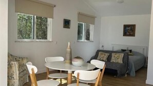 A modern, open-plan living space with a dining area featuring a round table and white chairs, a sofa, and a bed with a headboard. - Quinta Verde Algarve (Faro)