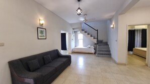 Ein modernes Wohnzimmer mit einem dunkelgrauen Sofa, einer Treppe, die zu einem Schlafzimmer führt, und einem Flur mit einer Tür.