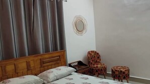Ein Schlafzimmer mit einem Holzkopfteil, einem Bett mit floralem Bettbezug, einem runden Spiegel an der Wand und zwei gemusterten Sesseln.