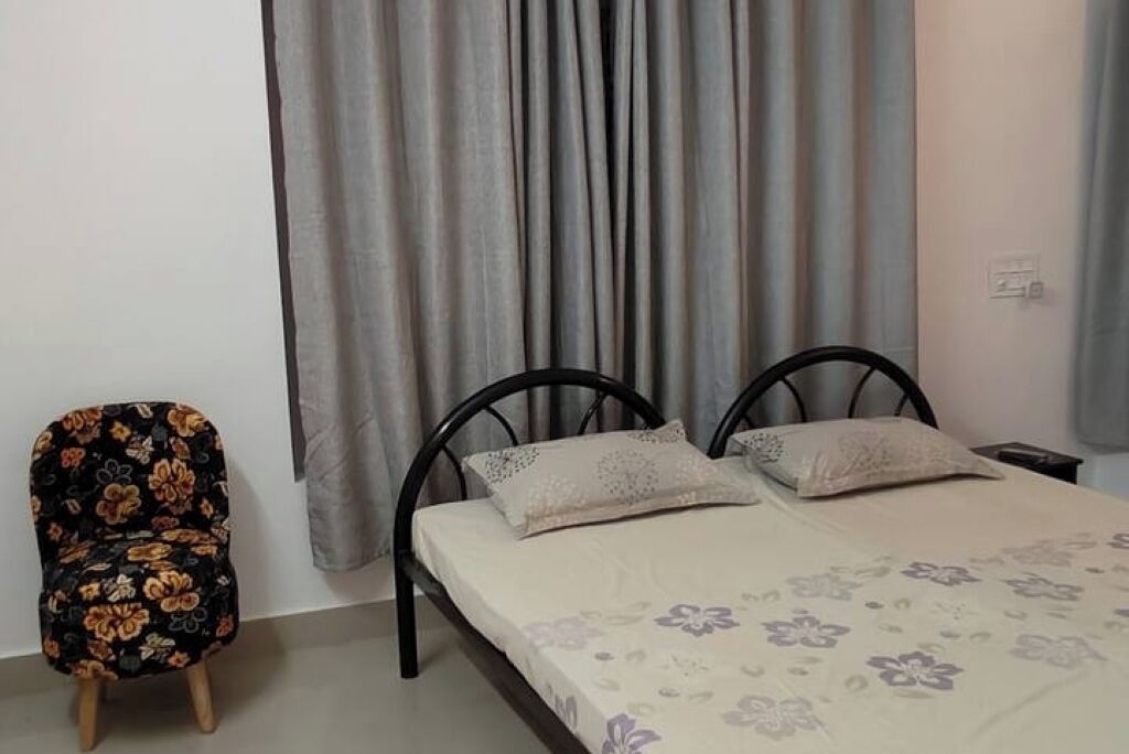 A bedroom with a bed, two pillows, a chair, and a curtain.