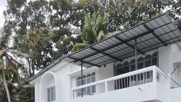 Ein weißes, zweistöckiges Gebäude mit Balkon, umgeben von üppiger Vegetation.