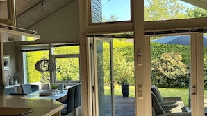 A modern kitchen with a built-in oven, a dining area with a table and chairs, and a sliding glass door leading to an outdoor patio with a garden view. - FeWoHuett - cozy vacation home in the Hüttener mountains near the Baltic Sea (Brekendorf)