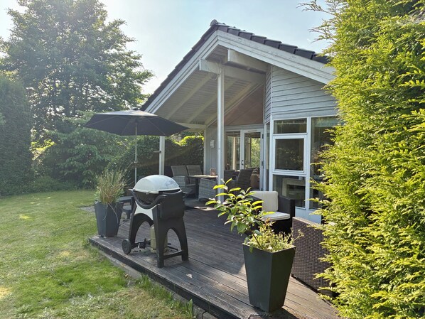Un patio techado con mobiliario exterior, una parrilla y plantas en macetas.
