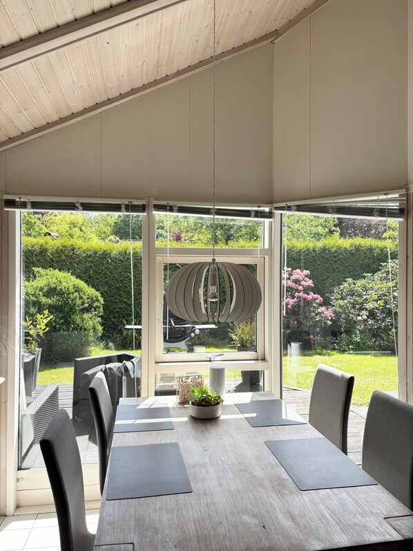 Un patio techado con una mesa y sillas, ventanas amplias y una lámpara colgante.
