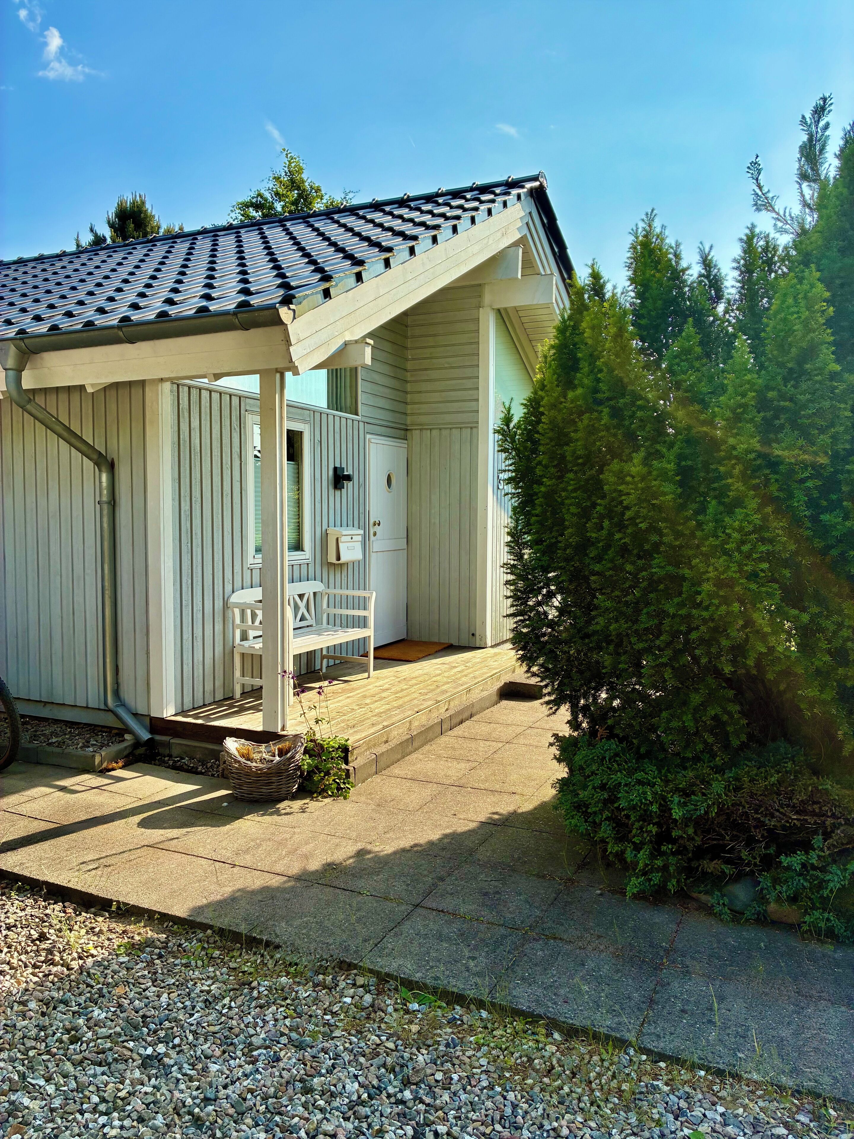 En inglasad veranda med en bänk, en dörr och en liten trädgårdsdel med en bänk och växter.