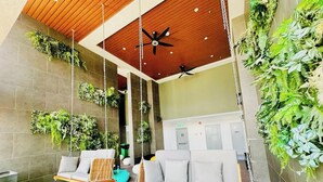 A modern lobby with a wooden ceiling, ceiling fans, a seating area with a swing chair, and vertical gardens.