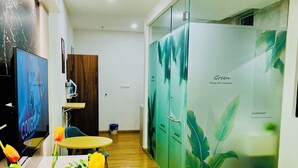 A hotel room with a bed, a TV, a desk with a vase of flowers, and a wardrobe with a green leaf design.