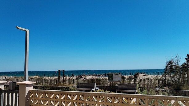 A beach view with a wooden fence, a street lamp, and a signboard. - Seafront apartment. All on foot (Saint-Cyprien)