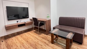 A modern living room with a flat-screen TV mounted on the wall, a wooden desk, a leather sofa, and a glass coffee table. - Basotel Hotel Indore (Indore)