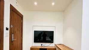 A room with a wooden floor, a mounted TV, a wooden bench, and a door with a lock. - Basotel Hotel Indore (Indore)