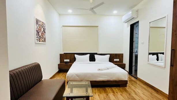 A modern hotel room with a bed, a seating area, a small table, and a ceiling fan. - Basotel Hotel Indore (Indore)