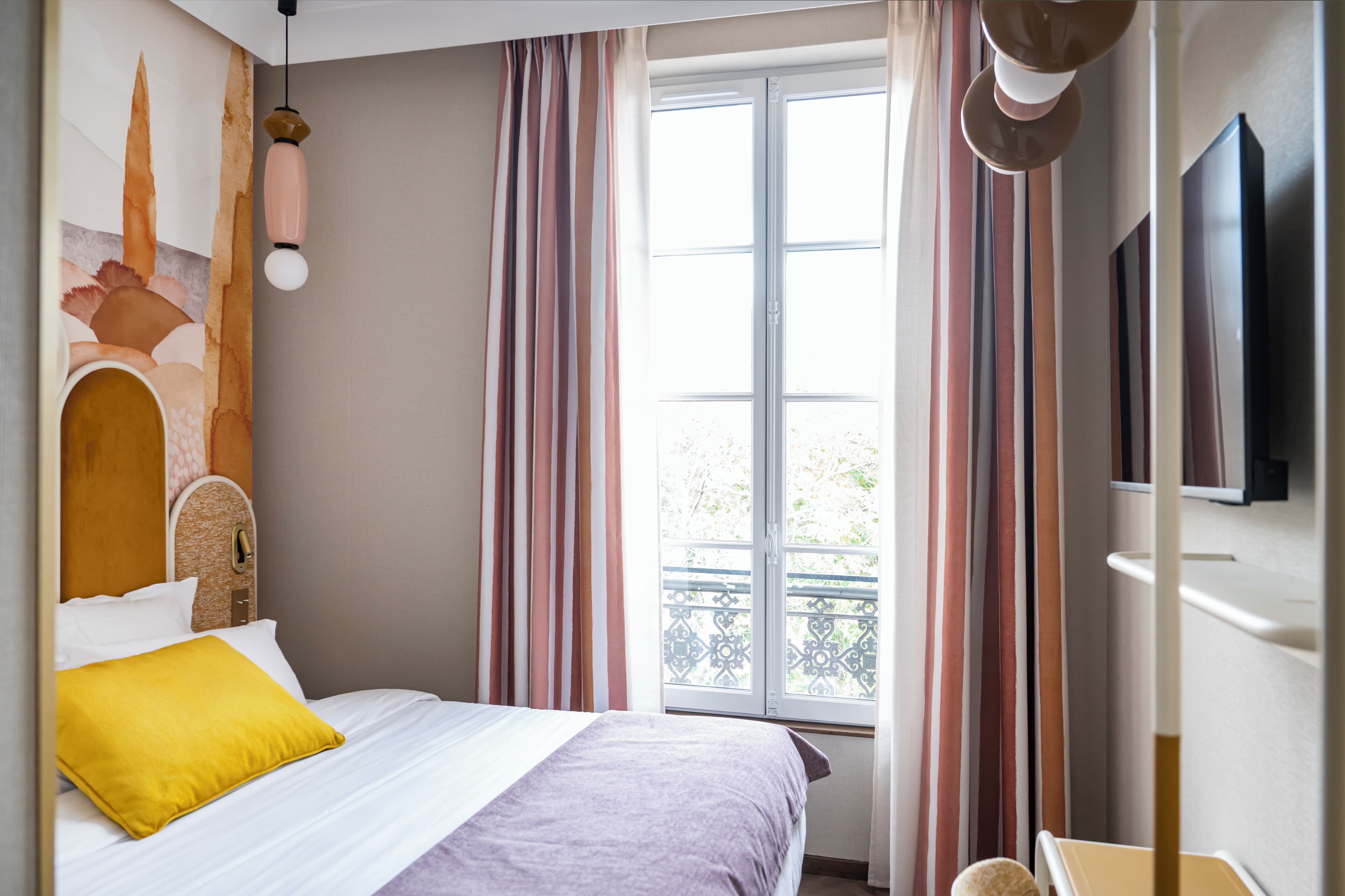A bedroom with a bed, a window with curtains, a wall-mounted TV, and a decorative wall piece.