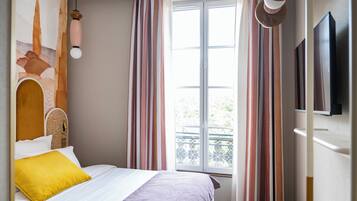 A bedroom with a bed, a window with curtains, a wall-mounted TV, and a decorative wall piece.