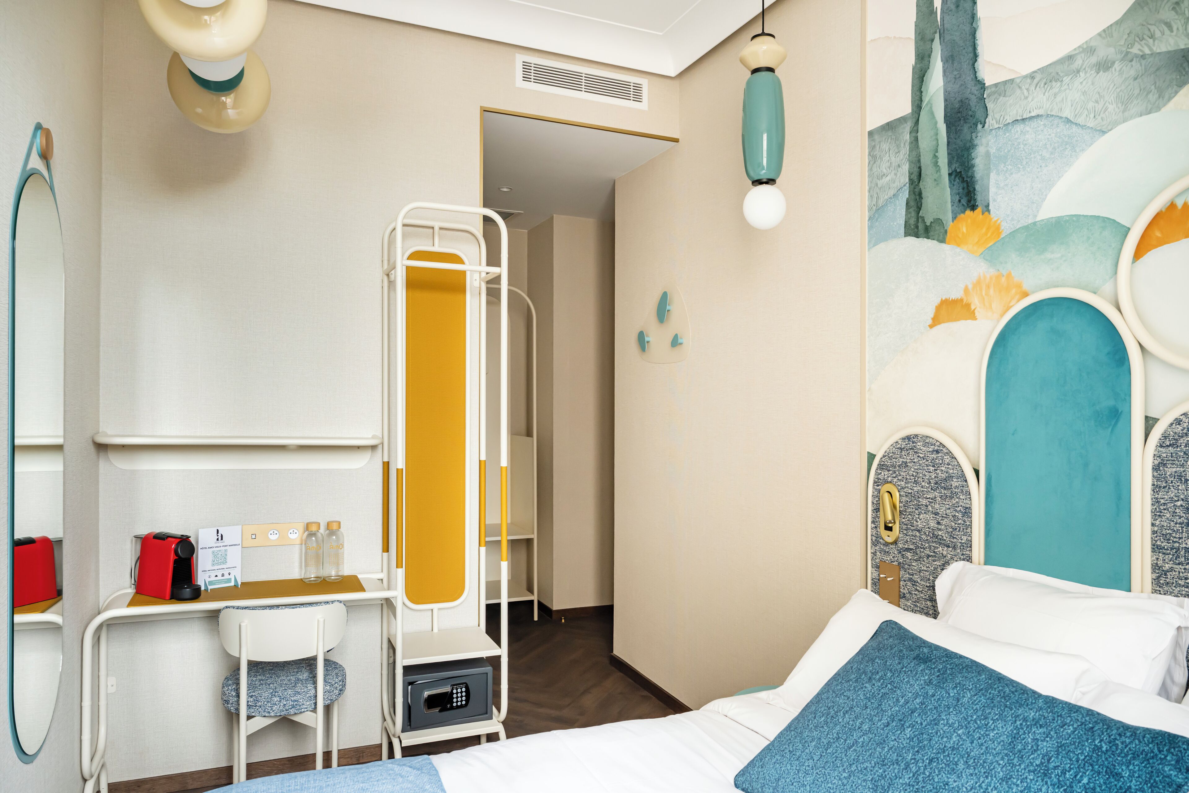 Quarto de hotel com uma cama, uma escrivaninha com cadeira, um espelho e banheiro com chuveiro.