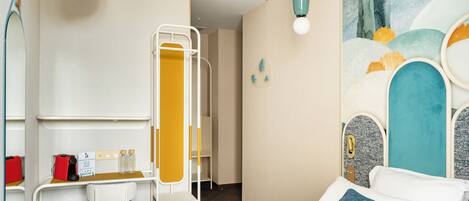 A hotel room with a bed, a desk with a chair, a mirror, and a bathroom with a shower.