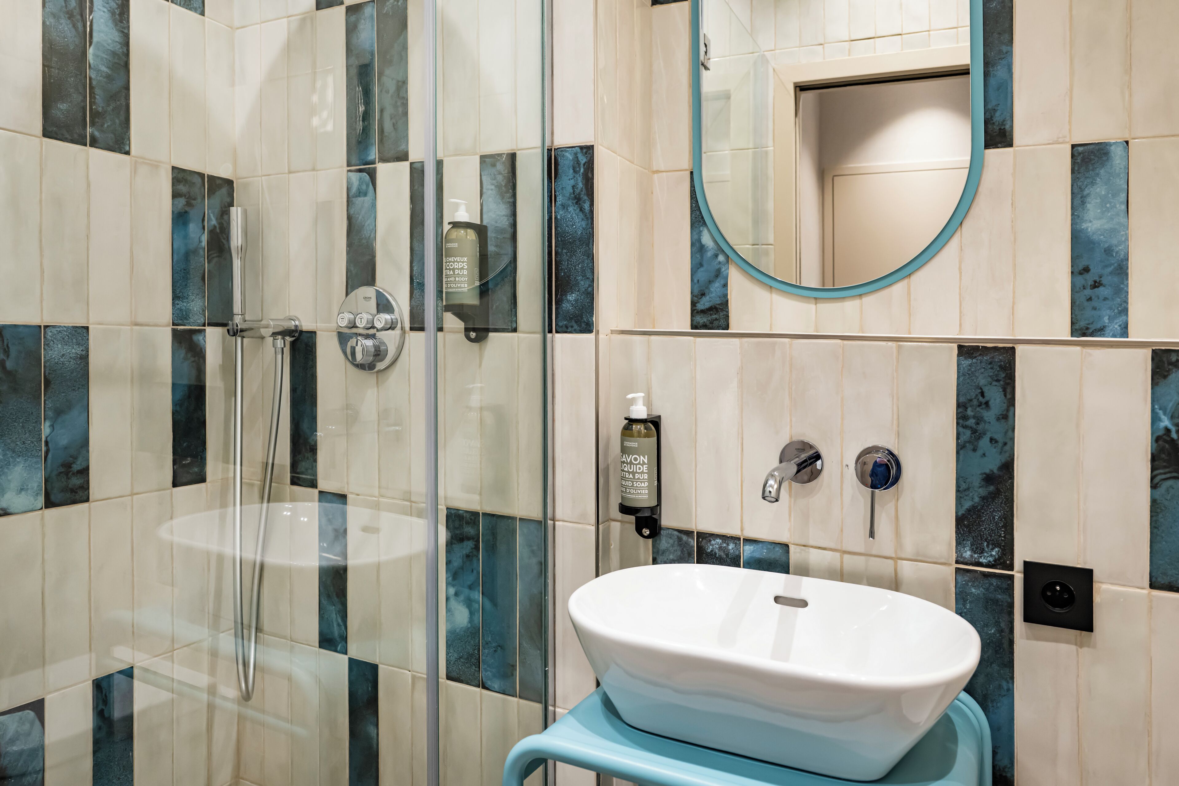 A bathroom with a glass-enclosed shower, a white sink, and a mirror with a blue frame.