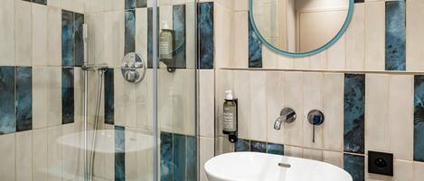 A bathroom with a glass-enclosed shower, a white sink, and a mirror with a blue frame.