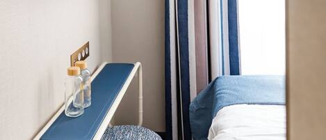 A modern hotel room with a flat-screen TV mounted on the wall, a small desk with a chair, and a bed with a blue headboard.