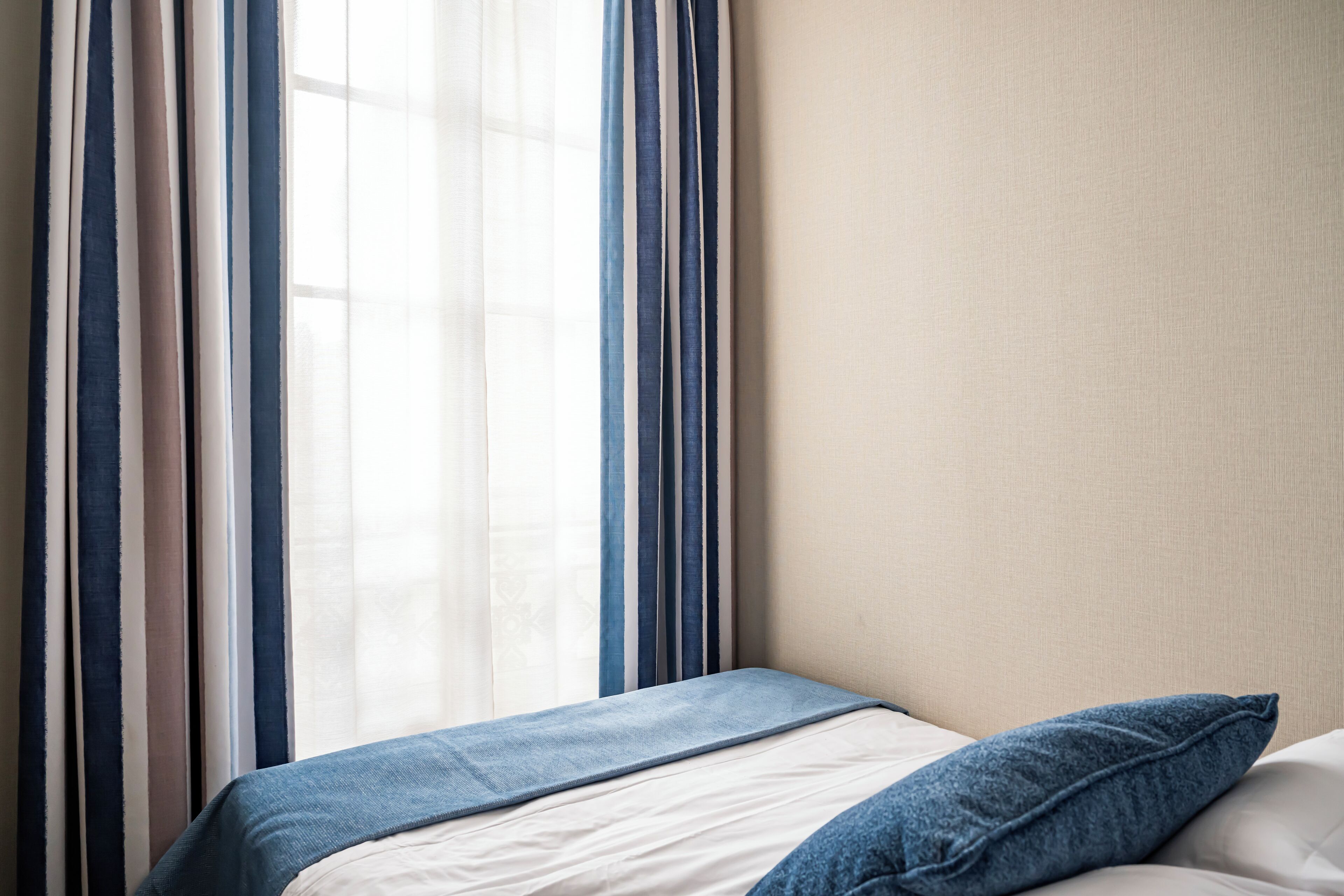 Una habitación de hotel con una cama, una ventana con cortinas y una pared lisa.