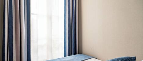 A hotel room with a bed, a window with curtains, and a plain wall.