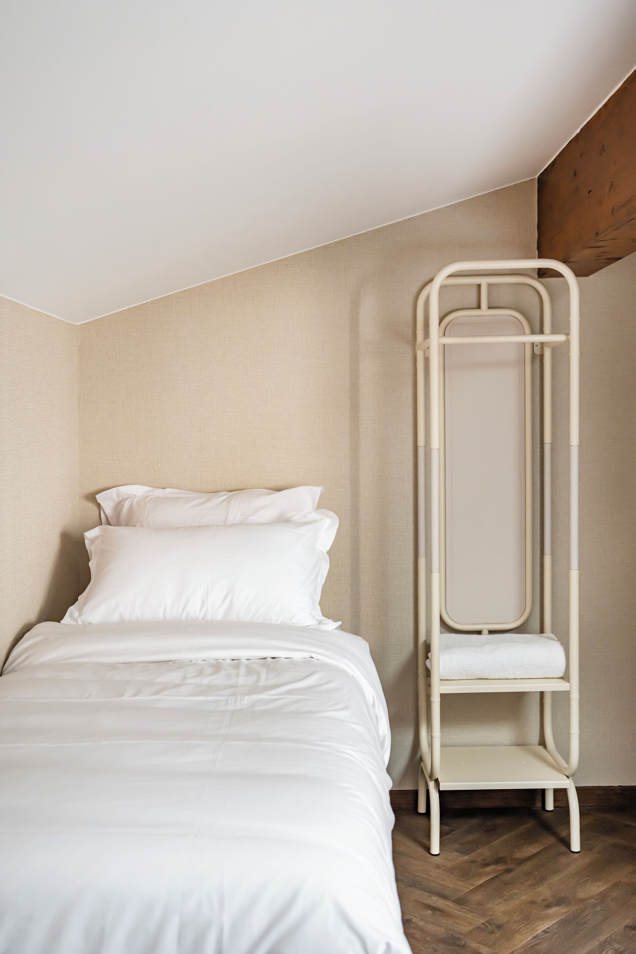 Una cama individual con ropa blanca en una habitación con suelo de madera y pared color beige.