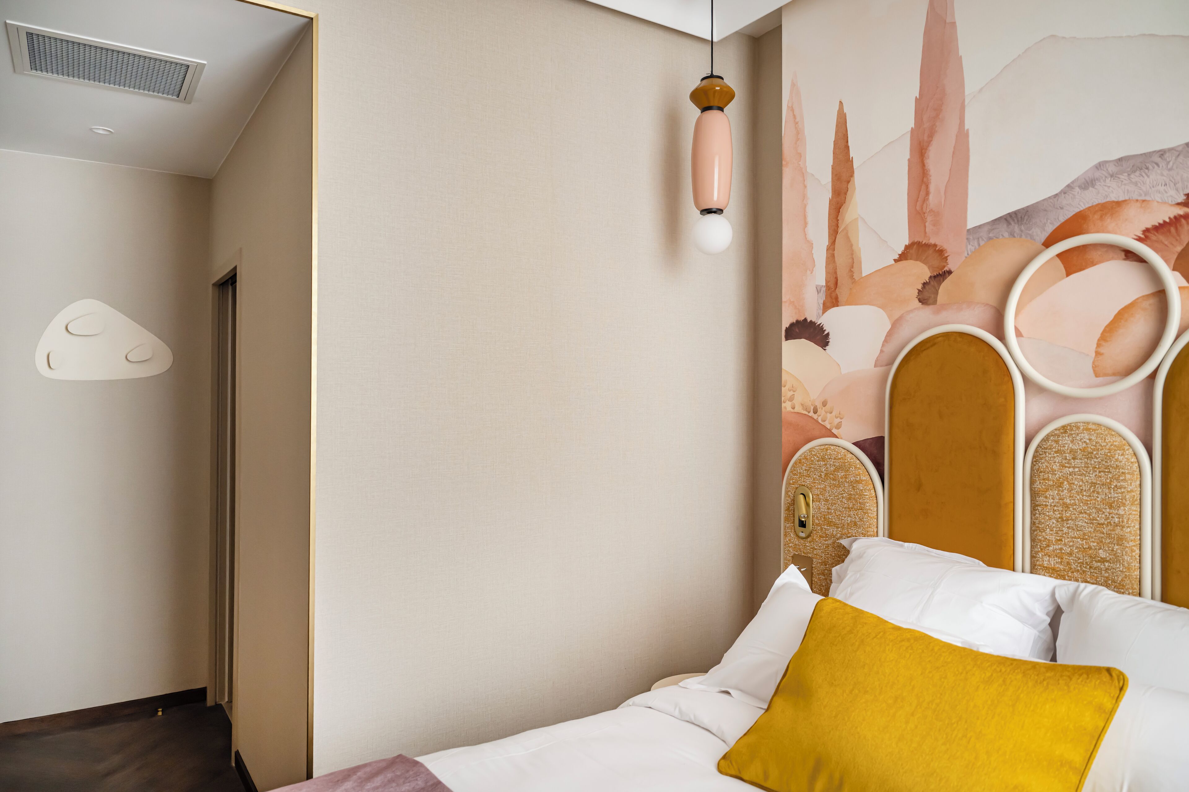 A modern hotel room with a bed, a unique headboard, and abstract wall art.