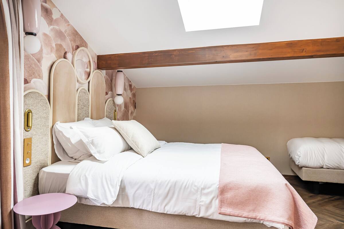 Une chambre à coucher avec un lit, des tables de chevet, une petite table ronde et une lucarne.