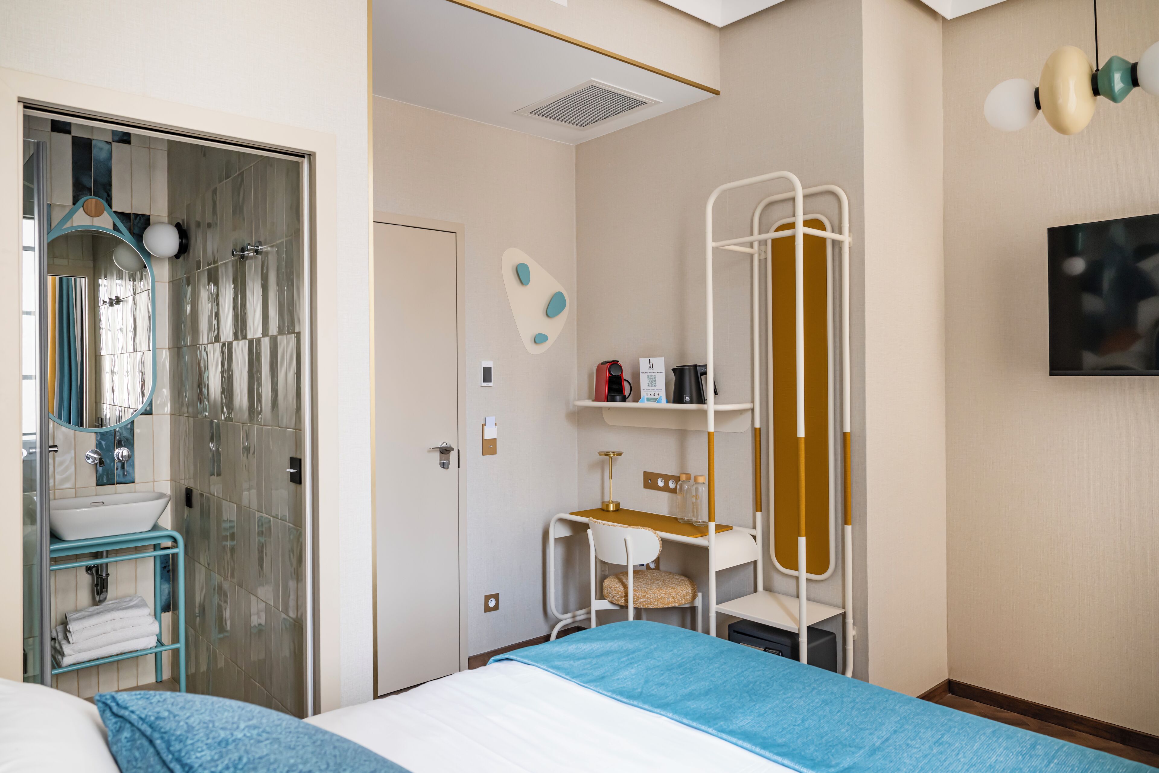 Une chambre d’hôtel comprenant un lit, une salle de bain avec un lavabo et un miroir, un bureau avec une chaise et une armoire.