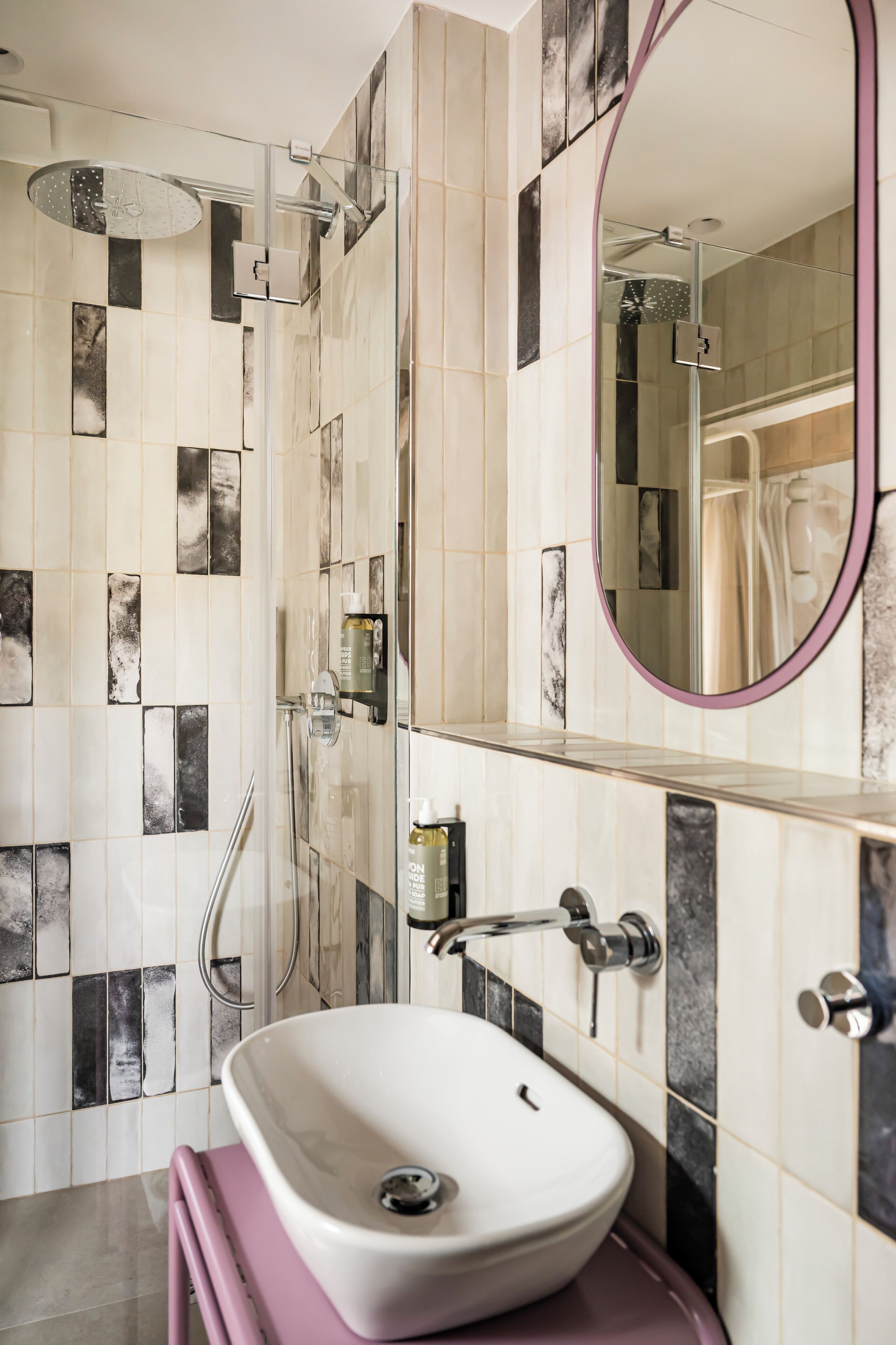A modern bathroom with a freestanding sink, a glass shower enclosure, and a mirror with a purple frame.