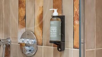 Baño con ducha, puerta de vidrio y una botella de loción corporal sobre un soporte negro.